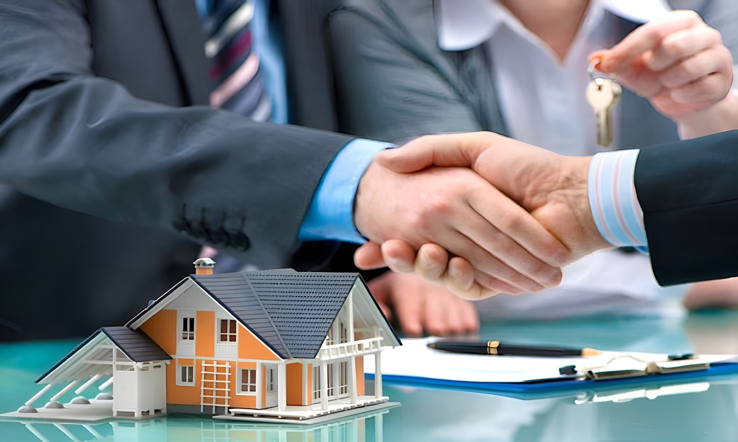 Dos personas de negocios dándose la mano sobre una mesa con una maqueta de casa.