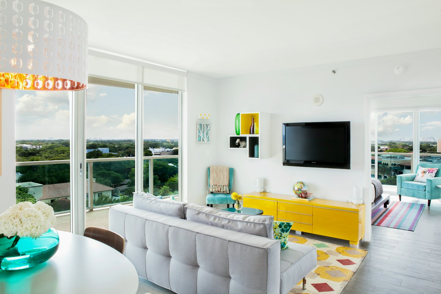 Sala de estar moderna con sofá gris y mueble de TV amarillo con vistas a la ciudad.